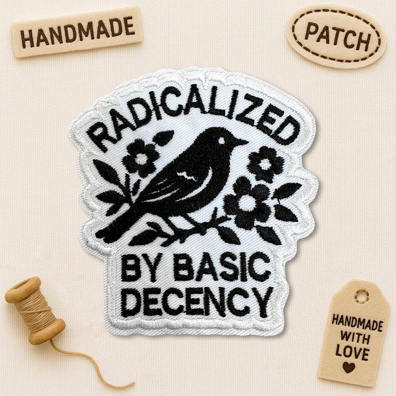 Pode incluir: Patch bordado com um p&aacute;ssaro preto empoleirado em um galho floral, com as palavras "RADICALIZED BY BASIC DECENCY" em branco. O patch &eacute; cercado por uma borda branca. Etiquetas adicionais dizem "HANDMADE" e "PATCH".