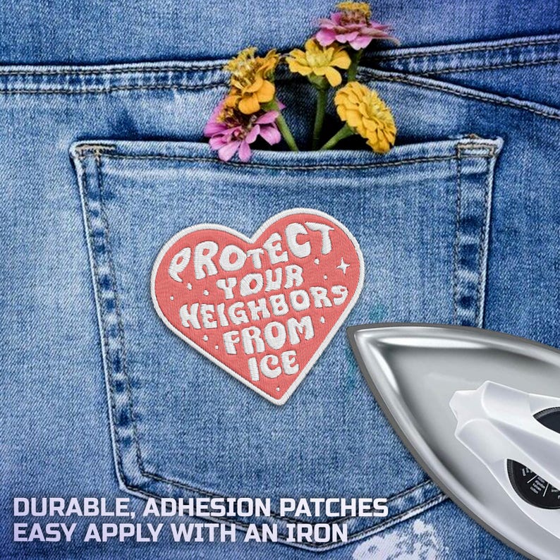 K&ouml;nnte beinhalten: Ein herzf&ouml;rmiger Aufn&auml;her mit dem Text "PROTECT YOUR NEIGHBORS FROM ICE" ist auf einer Jeans-Tasche angebracht. Die Tasche enth&auml;lt Blumen. Ein B&uuml;geleisen befindet sich in der unteren rechten Ecke.