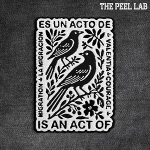 Peut inclure: Écusson brodé en noir et blanc avec deux oiseaux sur des branches et des éléments floraux. Le patch contient le texte "ES UN ACTO DE MIGRATION + LA MIGRACION VALENTIA + COURAGE IS AN ACT OF" et le texte "THE PEEL LAB".
