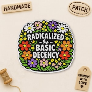 Peut inclure: Un écusson brodé rond avec une bordure florale blanche, orange, violette et rose. Le texte "RADICALIZED by BASIC DECENCY" est centré. Les étiquettes supplémentaires indiquent "HANDMADE", "PATCH" et "HANDMADE WITH LOVE".