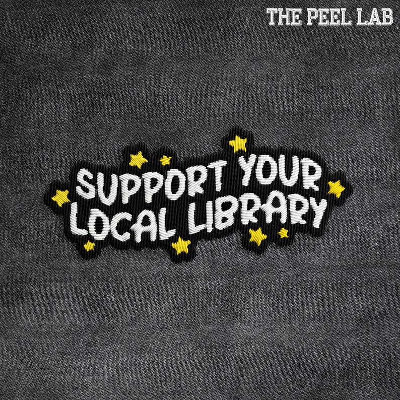 May include: Embroidered patch with the text "SUPPORT YOUR LOCAL LIBRARY" in white, outlined in black, and adorned with yellow star accents. The patch is set against a dark gray, textured background, with the text "THE PEEL LAB" at the top.