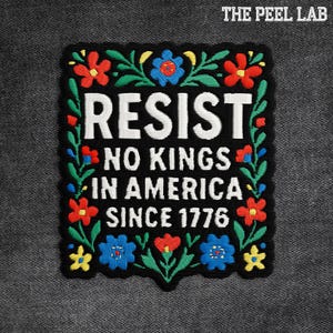 May include: Embroidered black patch with the word "RESIST" in white, along with "NO KINGS IN AMERICA SINCE 1776." The patch is framed with colorful floral embroidery in red, blue, green, and yellow.