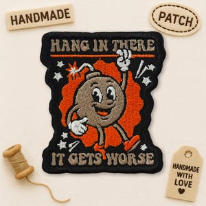 May include: Embroidered patch with a cartoon bomb character, the text "HANG IN THERE" and "IT GETS WORSE". The patch is black with orange and brown details. Includes a "PATCH" and "HANDMADE" tag.