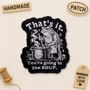 May include: Black embroidered patch featuring a frog chef stirring a pot with the text "That's it. You're going in the SOUP." Additional tags read "HANDMADE", "PATCH", and "HANDMADE WITH LOVE".