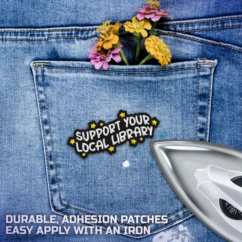 May include: Close-up of a denim pocket with a patch that reads "Support Your Local Library." The pocket contains colorful flowers. A silver iron is in the lower right corner. The text "Durable, Adhesion Patches, Easy Apply With An Iron" is at the bottom.