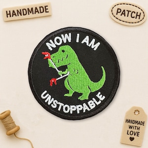 May include: Embroidered patch with a green dinosaur holding red tools, surrounded by the words "NOW I AM UNSTOPPABLE" in white on a black background. Includes a "PATCH" and "HANDMADE" tag.