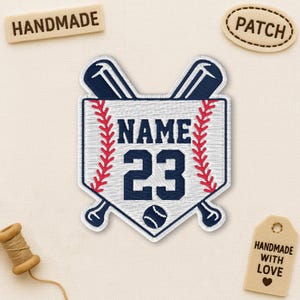 May include: Embroidered baseball patch with a white background, red stitching, and navy blue accents. The patch features the word "NAME" above the number "23" and a baseball graphic. Two crossed baseball bats are at the top. The patch is surrounded by red stitching.