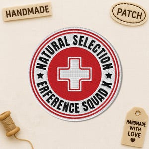 May include: Embroidered patch with the words "NATURAL SELECTION REFERENCE SQUAD X" in a circular design. The patch features a red background with a white cross symbol. Additional tags read "HANDMADE" and "PATCH".