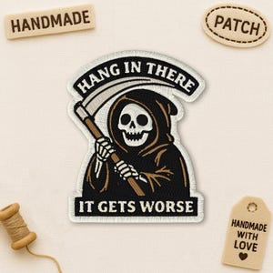 May include: Embroidered patch depicting the Grim Reaper with a scythe, with the words "HANG IN THERE" and "IT GETS WORSE". Additional tags read "HANDMADE" and "PATCH".