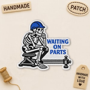 May include: Embroidered patch featuring a skeleton wearing a blue hard hat, seated and deep in thought. The patch reads "WAITING ON PARTS" in blue lettering. Additional tags read "HANDMADE" and "PATCH".