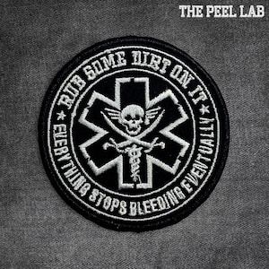 May include: A black and white embroidered patch with the text "RUB SOME DIRT ON IT" and "EVERYTHING STOPS BLEEDING EVENTUALLY". The patch features a skull and crossbones design within a star of life symbol. The Peel Lab logo is in the top right corner.