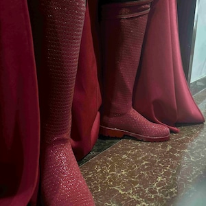 May include: A pair of knee-high, red boots with a textured, glittery finish. The boots are paired with a matching red cape, creating a cohesive and striking ensemble. The boots appear to be made of a durable material, suitable for cosplay or costume events.