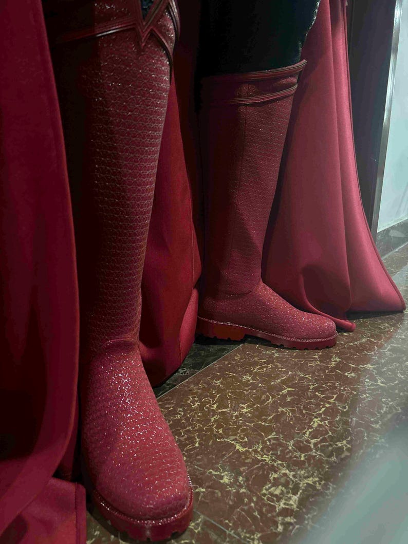 May include: A pair of knee-high, red boots with a textured, glittery finish. The boots are paired with a matching red cape, creating a cohesive and striking ensemble. The boots appear to be made of a durable material, suitable for cosplay or costume events.
