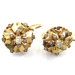 Könnte beinhalten: Ein Paar goldene Ohrringe mit einem kreisförmigen, facettierten Design, einem zentralen klaren Stein und kleinen weißen Saatperlen. Die Ohrringe haben eine metallisch gelbe Oberfläche und sind mit gebogenen Ohrhaken versehen.