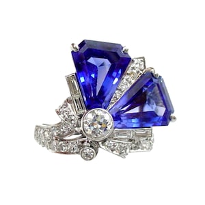 May include: A striking ring featuring two large, triangular, deep blue gemstones, accented with smaller diamonds and set in a silver or white gold band. The ring has a unique, fan-like design with a central, round diamond.