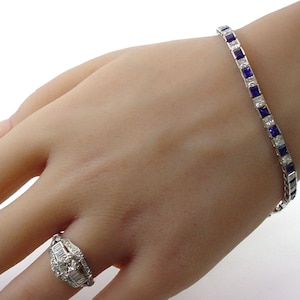 May include: A silver-toned metal bracelet featuring alternating square-cut deep blue sapphires and clear white diamonds, paired with a matching silver-toned ring set with a central round diamond surrounded by baguette and round accent diamonds.
