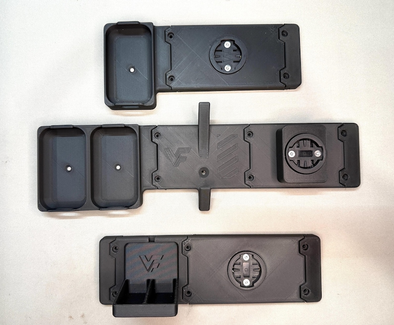 May include: Three black matte 3D-printed mounts with integrated circular locking mechanisms. The top mount has one rectangular compartment, the middle has two, and the bottom has a small dual-bin section. Each features the VF logo embossed.