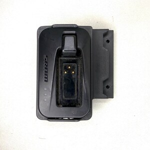 May include: A black SRAM battery charger featuring a rectangular housing with a central recessed port containing three gold-colored electrical contact pins. The unit includes a side mounting bracket with two circular holes and the SRAM logo printed on the front.