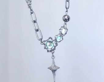 Op de afbeelding: Zilverkleurige ketting met een mix van schakels en decoratieve elementen. Het heeft lichtblauwe-groene iriserende stenen en een stervormige hanger met een kleine, heldere edelsteen. Het ontwerp is ingewikkeld en delicaat.
