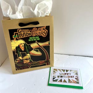 Sacola de presente e cartão comemorativo com a história em quadrinhos do Arqueiro Verde e da Canário Negro