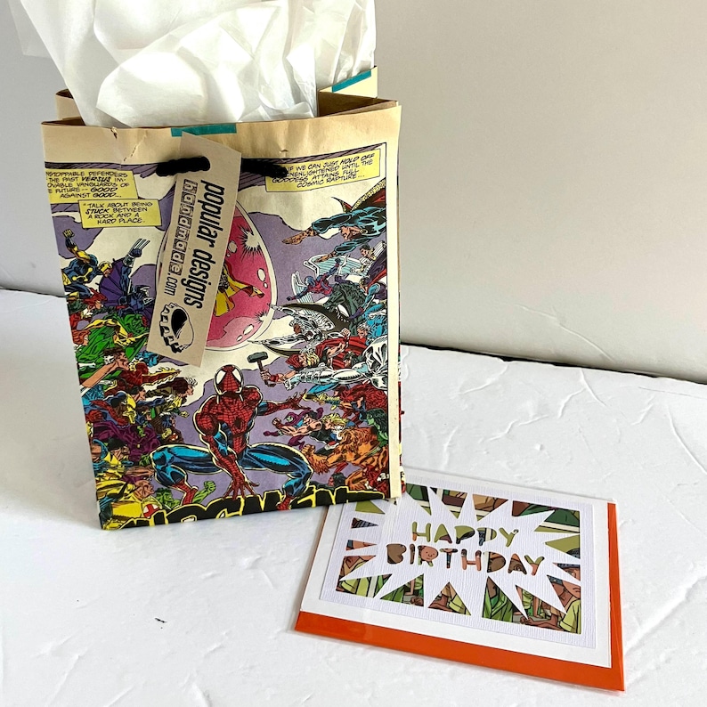 Pu&ograve; includere: Un sacchetto regalo realizzato con pagine di fumetti riciclate raffigurante Spider-Man e vari supereroi, con carta velina bianca all'interno e un'etichetta con la scritta popular designs. Accanto c'&egrave; un biglietto con il testo HAPPY BIRTHDAY.