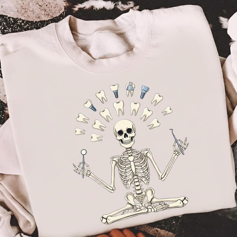 May include: Cream-coloured sweatshirt with a dental-themed skeleton design. The skeleton is surrounded by teeth and dental tools. The graphic includes a skull, teeth, and dental implants, creating a unique and humorous design.