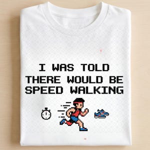 Może przedstawiać: Biały t-shirt z grafiką pixel art przedstawiającą biegnącą osobę, stoper i parę butów sportowych. Tekst wydrukowany czarną, pikselową czcionką brzmi: I WAS TOLD THERE WOULD BE SPEED WALKING. Koszulka posiada subtelny wzór geometryczny.