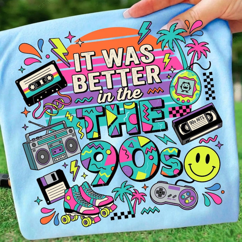 May include: A light blue t-shirt featuring a colorful graphic with the text "IT WAS BETTER in the 90s". The design includes illustrations of a cassette tape, a boombox, a floppy disk, roller skates, a handheld game, a VHS tape, and a smiley face.