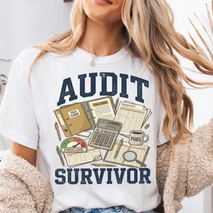 Può includere: T-shirt bianca con la scritta "AUDIT SURVIVOR" in blu navy. La grafica include una calcolatrice, documenti fiscali, una tazza di caffè e un indicatore del livello di stress. Un design divertente per contabili e revisori.
