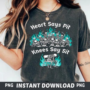 May include: Dark gray t-shirt with the text "Heart Says Pit Knees Say Sit" and a graphic of skeletons. The graphic includes skeletons in a group and one sitting in a chair, with teal flames.