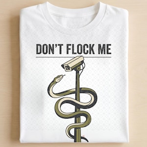 May include: A white t-shirt featuring a graphic print of a green snake coiled around a security camera pole. Above the illustration, the text reads DON'T FLOCK ME in black capital letters. The shirt has a subtle, repeating geometric pattern.