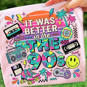 May include: A light pink t-shirt featuring a colorful 1990s-themed graphic with the text IT WAS BETTER in the 90s. The design includes a cassette tape, a boombox, a floppy disk, roller skates, a digital pet, a VHS tape, and a game controller.
