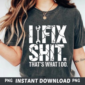 Puede incluir: Camiseta gris oscuro con el texto "I FIX SHIT. THAT'S WHAT I DO." en fuente blanca desgastada. Un gráfico de llave inglesa está incorporado en el texto. Es una prenda de vestir informal.