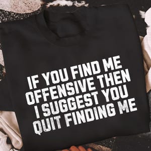 Op de afbeelding: Zwart sweatshirt met witte tekst: "IF YOU FIND ME OFFENSIVE THEN I SUGGEST YOU QUIT FINDING ME." De crewneck sweatshirt is gemaakt van een zacht materiaal.