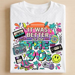May include: A white t-shirt featuring a colorful graphic print with the text "IT WAS BETTER in the 90s". The design includes a cassette tape, boombox, floppy disk, roller skates, handheld game, smiley face, and video game controller.
