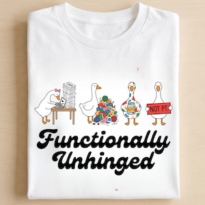 Peut inclure: T-shirt blanc avec un motif de quatre oies de dessin animé dans différentes situations. L'une est devant un ordinateur, une autre avec de la laine, une troisième avec de la peinture et la dernière avec un panneau "NOT PT". Le texte "Functionally Unhinged" est en dessous.