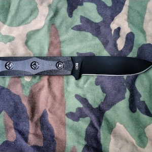 May include: A black knife with a textured handle and a straight blade. The knife has a full tang construction and is marked with "EK51" on the blade. The knife is set against a camouflage background.