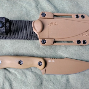 May include: A tan KA-BAR BK-18 knife with a matching sheath and black nylon belt loop. The knife has a fixed blade and a tan handle. The sheath has the KA-BAR logo and the initials "JD".