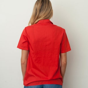 Op de afbeelding: Een rood, kort mouwig overhemd met knopen en een kraag.