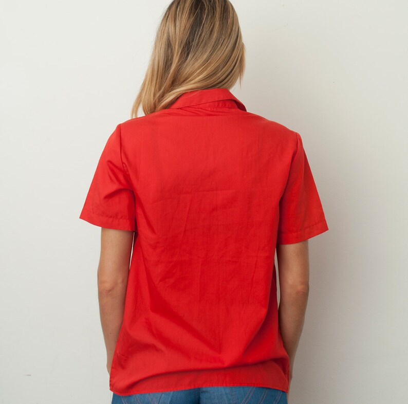 Op de afbeelding: Een rood, kort mouwig overhemd met knopen en een kraag.