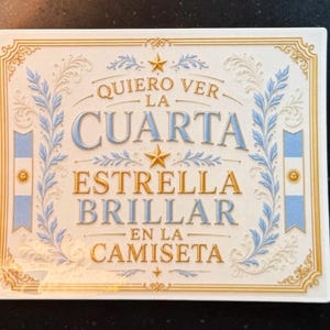 May include: A rectangular white ceramic plaque featuring gold and light blue decorative borders and floral accents. The text reads: QUIERO VER LA CUARTA ESTRELLA BRILLAR EN LA CAMISETA, accompanied by two gold stars and two vertical Argentine flag motifs.