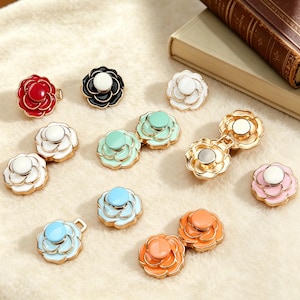 May include: A selection of flower-shaped buttons in a range of colours: red, black, white, mint green, light blue, orange, and pink. Each button has a gold-coloured trim and a white centre. Some are designed as clasps.