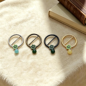 Pode incluir: Quatro broches decorativos em forma de anel com um design de flor e contas. Os broches são em prata, bronze, preto e ouro. Cada broche tem uma flor verde e uma conta de cor diferente: azul, verde, verde e amarelo.