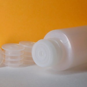 May include: A white plastic bottle with a white plastic cap and several white plastic bottle stoppers.