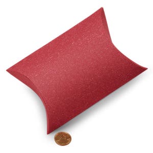 May include: A red pillow box made of textured paper. The box is empty and is sitting on a white surface.