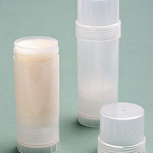 May include: Three clear, cylindrical deodorant containers. One container is open, revealing a solid, off-white product. The other two containers are closed, with white caps. The containers are made of translucent plastic and sit on a light green surface.