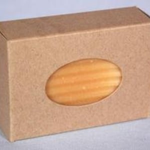 May include: A brown cardboard box with a window showing a bar of soap. The soap is a light yellow color and has a textured surface.