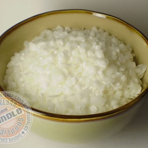 May include: A close-up of a bowl filled with white wax flakes. The bowl is a light brown color with a darker brown rim.