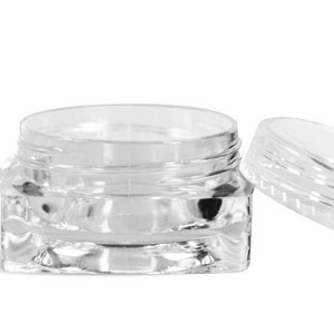 May include: A clear, small, round jar with a matching lid. The jar is made of transparent plastic and has a ribbed design around the sides. The lid is off to the side, revealing the inside of the jar.