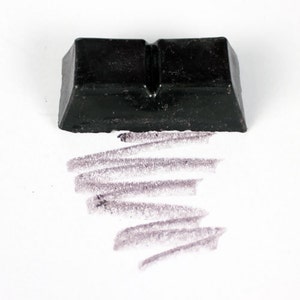 May include: A black rectangular block of charcoal for drawing, with a line of charcoal drawn on a white surface.